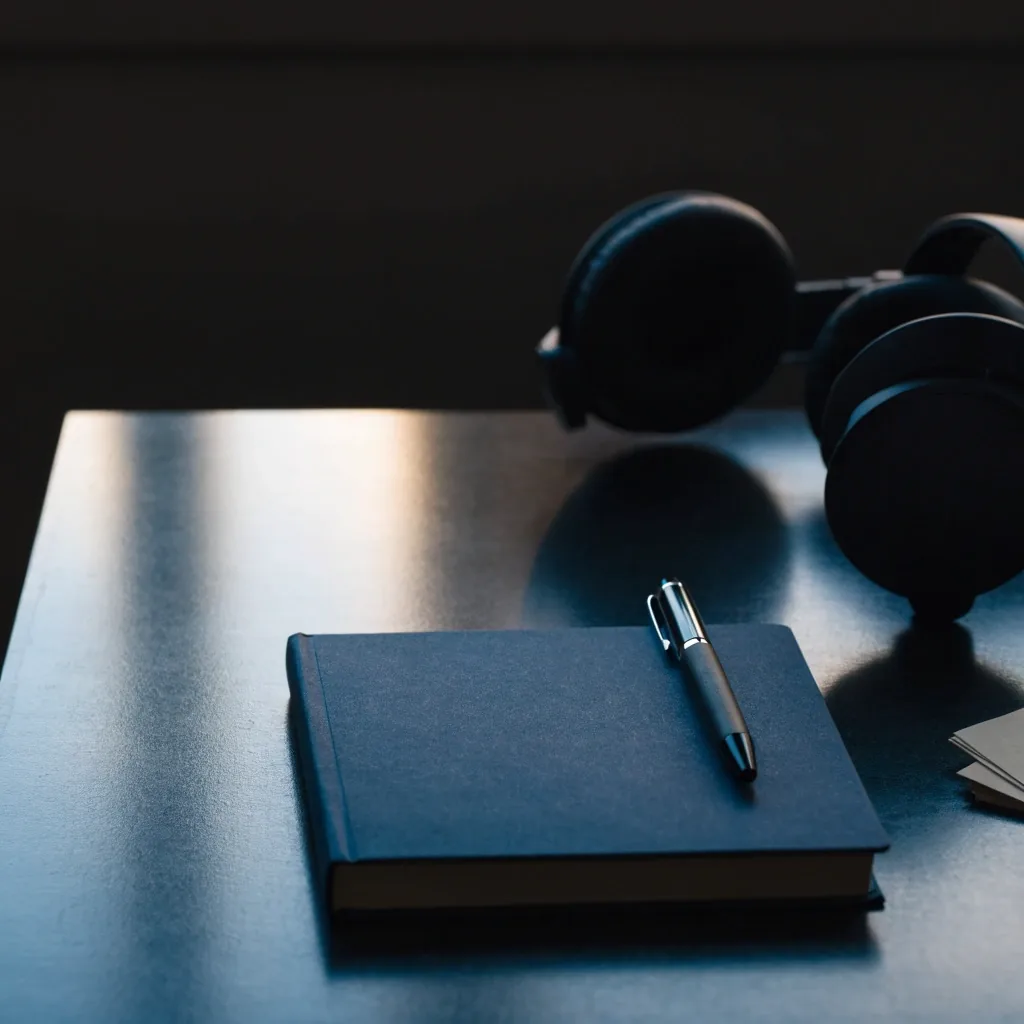 Top-down view of a charcoal desk with a closed notebook, pen, and headphones in cool daylight
